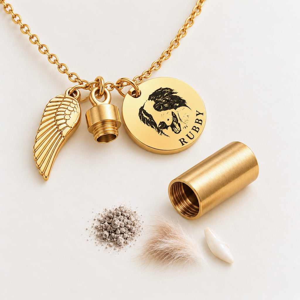 Gold pet urn necklace featuring an engraved dog portrait medallion, a miniature ashes capsule, an angel wing charm, and open capsule components with sample pet hair, ashes, and a tooth on a white surface