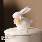 Close-up of the ivory rabbit figure with hand-sculpted pink flowers and green leaves on the ceramic urn lid