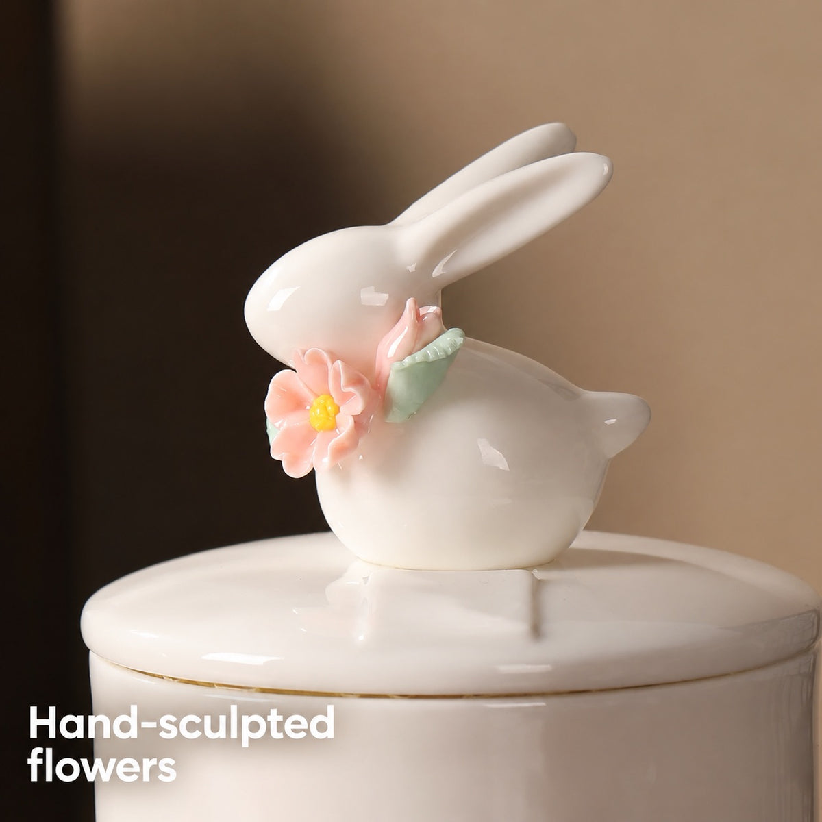 Close-up of the ivory rabbit figure with hand-sculpted pink flowers and green leaves on the ceramic urn lid