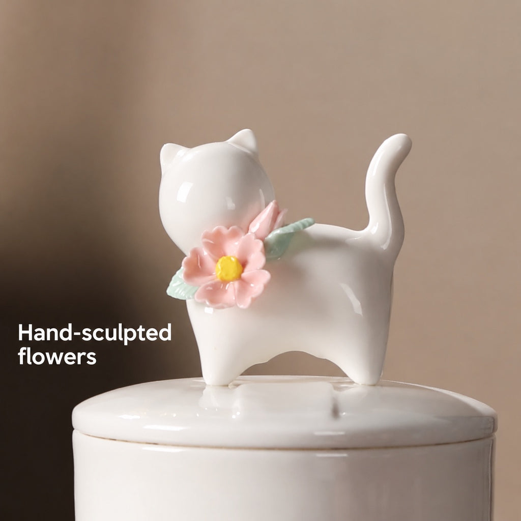 Close-up of the ivory cat figure with hand-sculpted pink flowers and green leaves on the ceramic urn lid