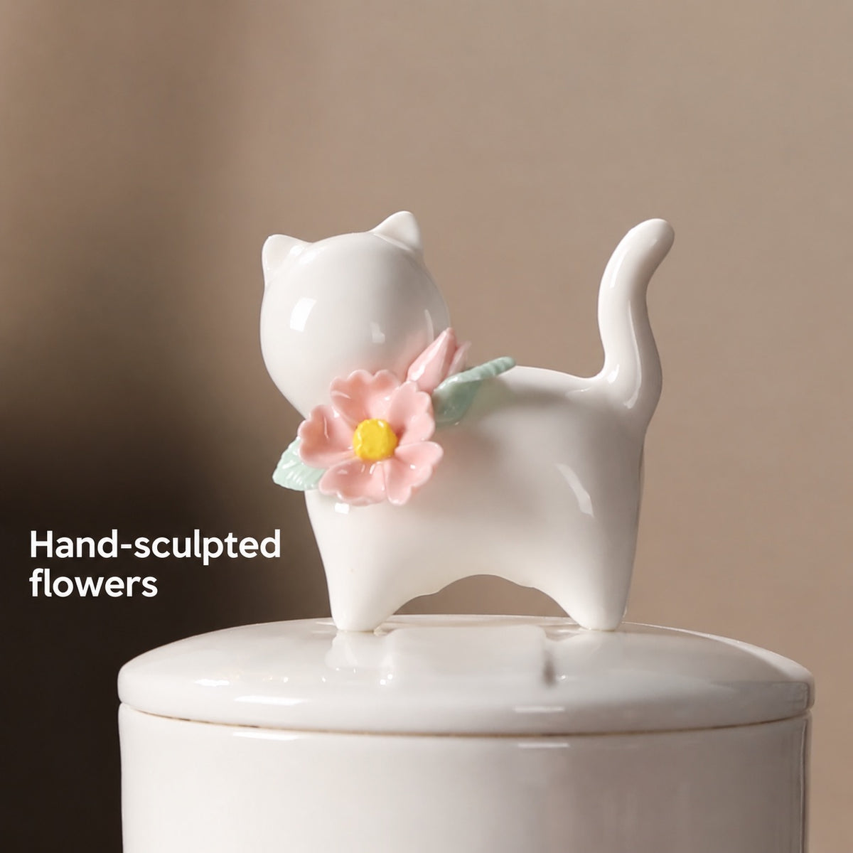 Close-up of the ivory cat figure with hand-sculpted pink flowers and green leaves on the ceramic urn lid