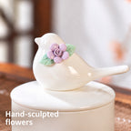 Close-up of the ceramic bird figure and hand-sculpted purple flower with green leaves on the urn lid