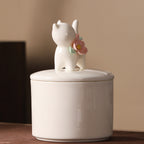Rear view of a large ivory ceramic cat memorial urn with a standing cat figure and floral decoration on the lid