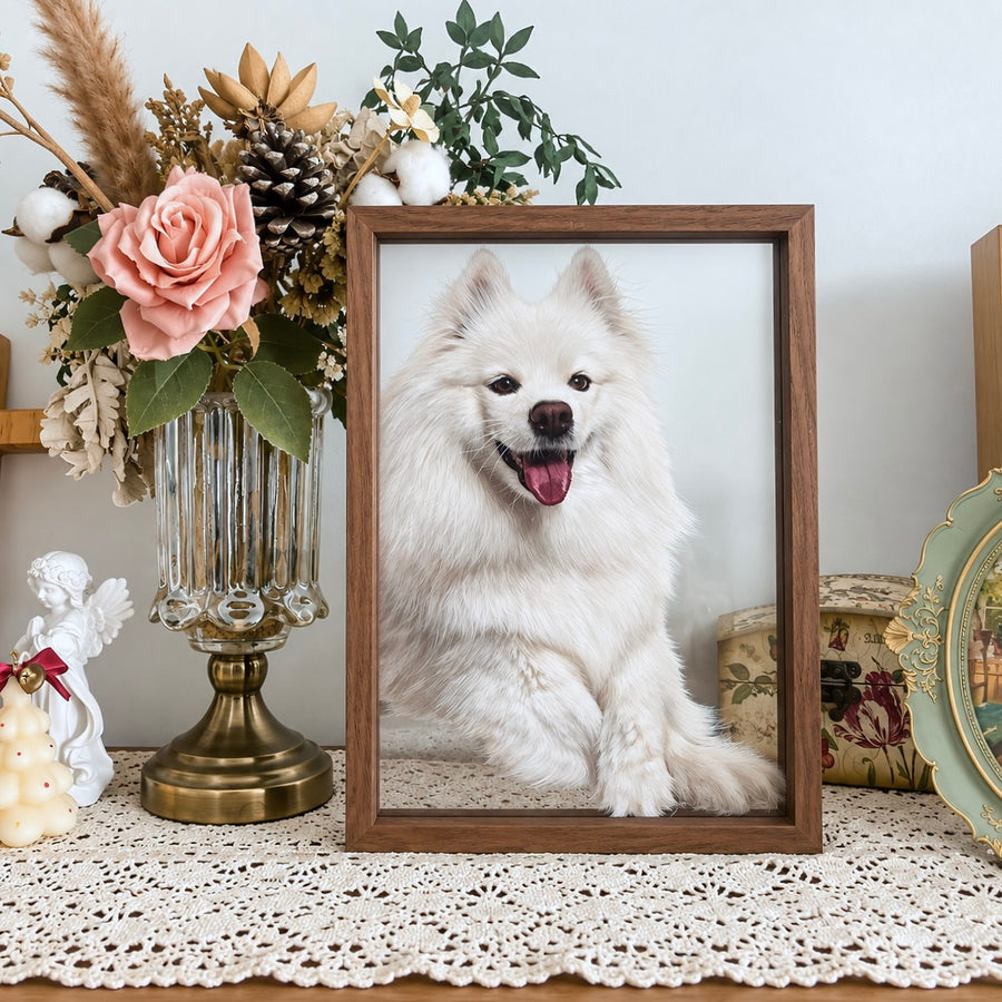 Custom framed pet portrait of a smiling fluffy white dog displayed on a table with vintage floral decor, lace tablecloth, and rose flowers.