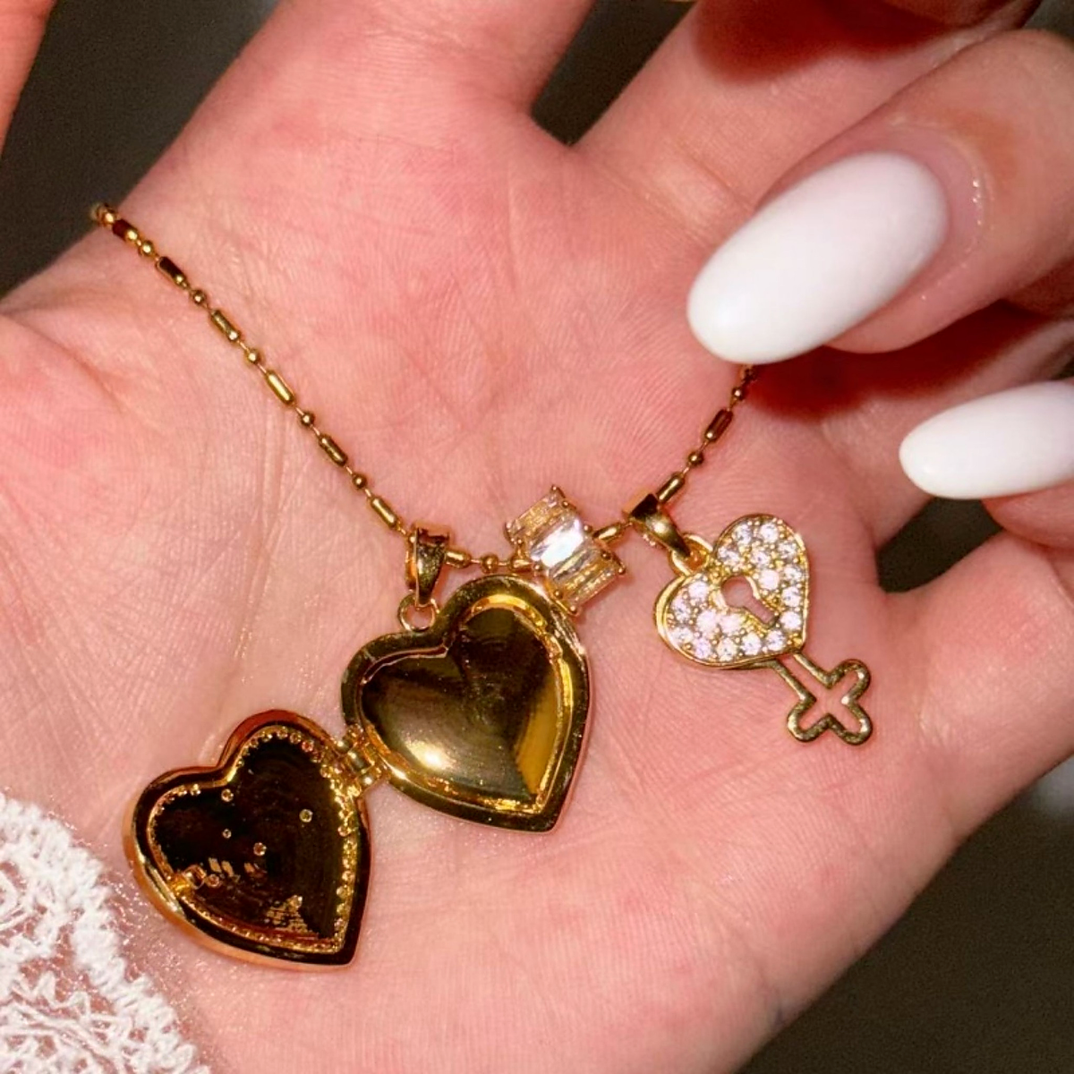 Open gold heart photo locket necklace with empty photo recess and zircon key charm held in a hand