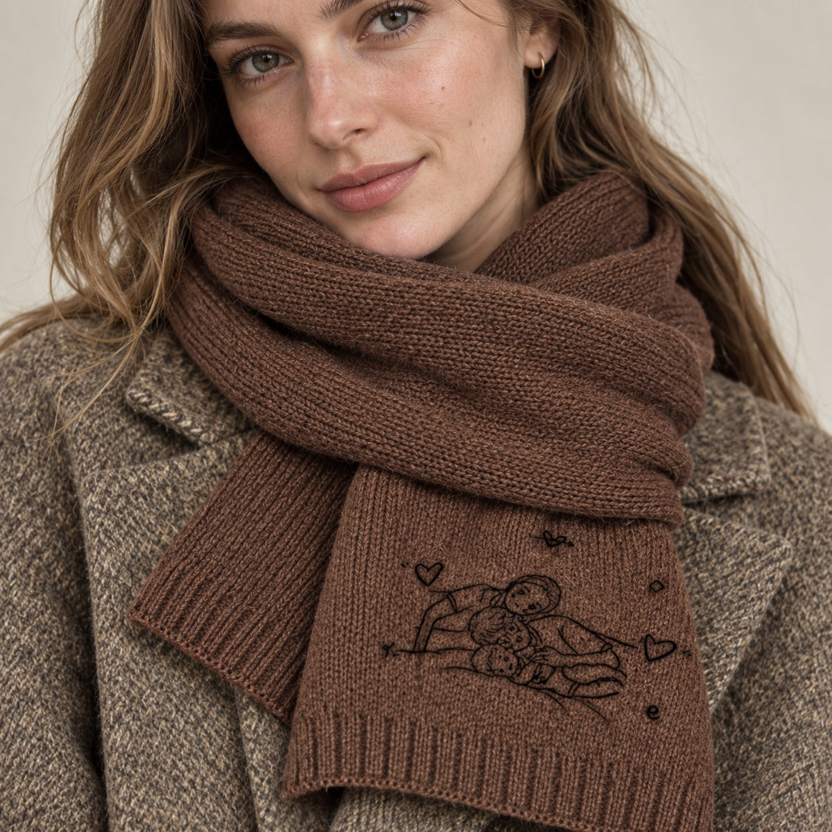 Woman wearing a brown knit scarf embroidered with a family line portrait, small hearts and decorative details