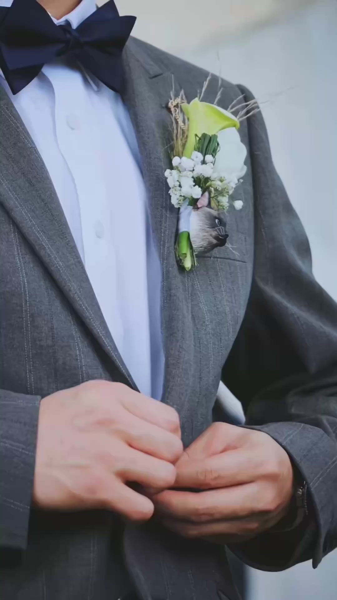 Close-up of personalized handmade pet portrait wedding flowers. It demonstrates a miniature plaster cat head boutonniere for the groom and a white floral wrist corsage for the bride. Ideal for cat lovers seeking unique ways to honor their pets during the wedding ceremony.