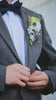Close-up of personalized handmade pet portrait wedding flowers. It demonstrates a miniature plaster cat head boutonniere for the groom and a white floral wrist corsage for the bride. Ideal for cat lovers seeking unique ways to honor their pets during the wedding ceremony.