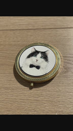 Video displaying a custom 3D embossed tuxedo cat compact mirror with a black bow tie, a luxury vintage makeup accessory by Memopaw.