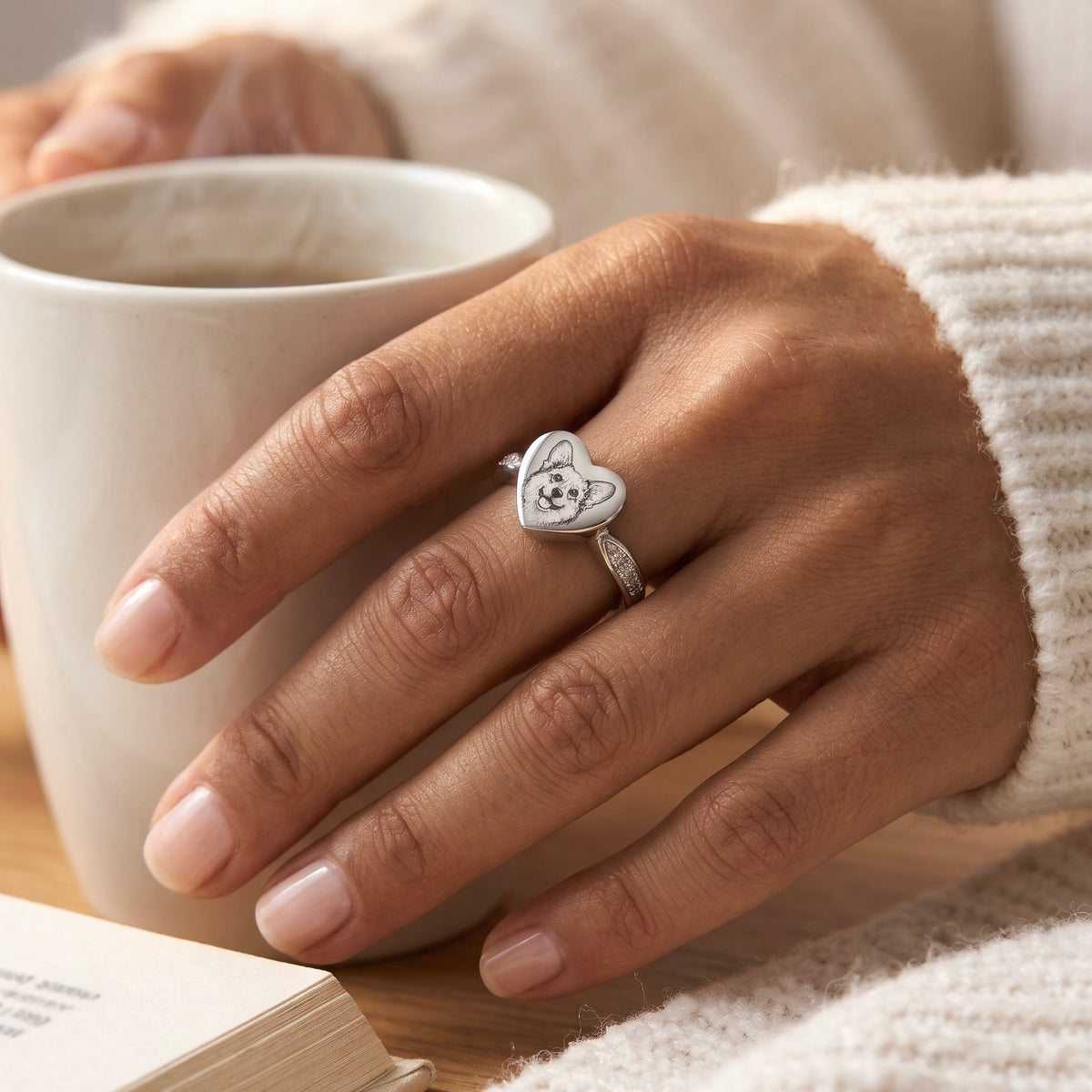 Silver heart memorial ring with a custom small-dog portrait worn beside a book and cup