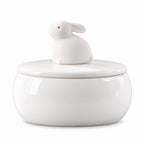 White ceramic memorial urn with a sitting rabbit figure and small red eye on the lid