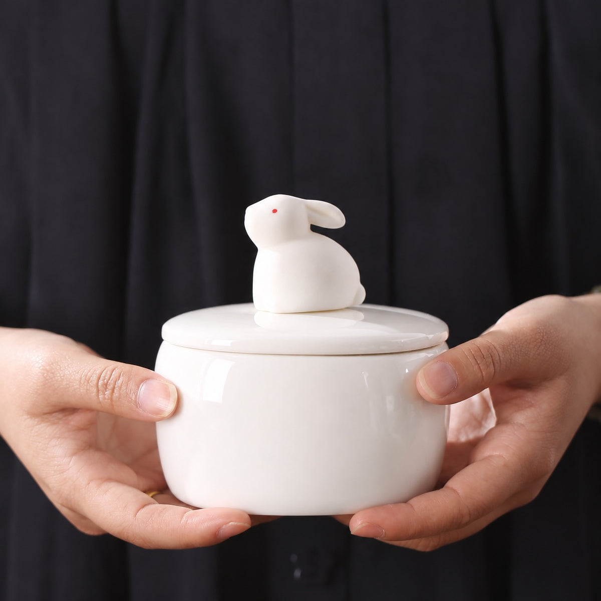 White ceramic sitting rabbit memorial urn held carefully in two hands against a dark background