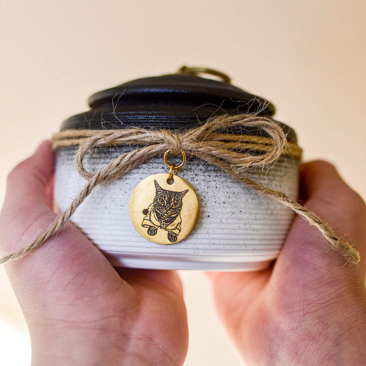 Small ceramic cat ashes urn held in two hands with a personalized cat photo memorial tag
