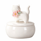 Small ivory ceramic cat memorial urn with a standing cat figure, pink flower and green leaves on the lid