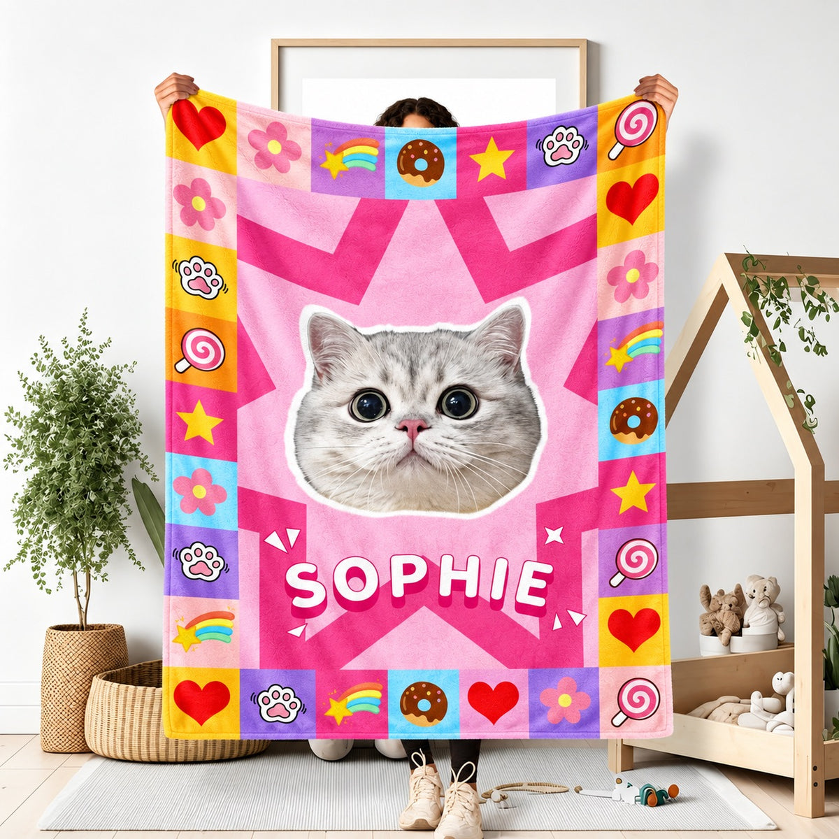 Person holding a pink cat portrait blanket with a large star, colorful icons and the name Sophie
