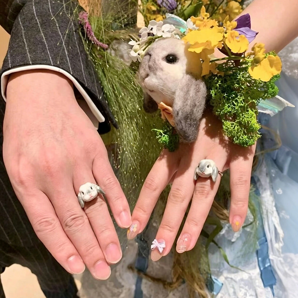A bride and groom holding hands during their ceremony, wearing bespoke 3D rabbit portrait rings custom hand-sculpted to match the adorable companion nestled in the yellow wedding bouquet, serving as a luxury sentimental keepsake.