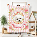 Person holding a pink striped blanket with a small white dog portrait, roses and floral motifs